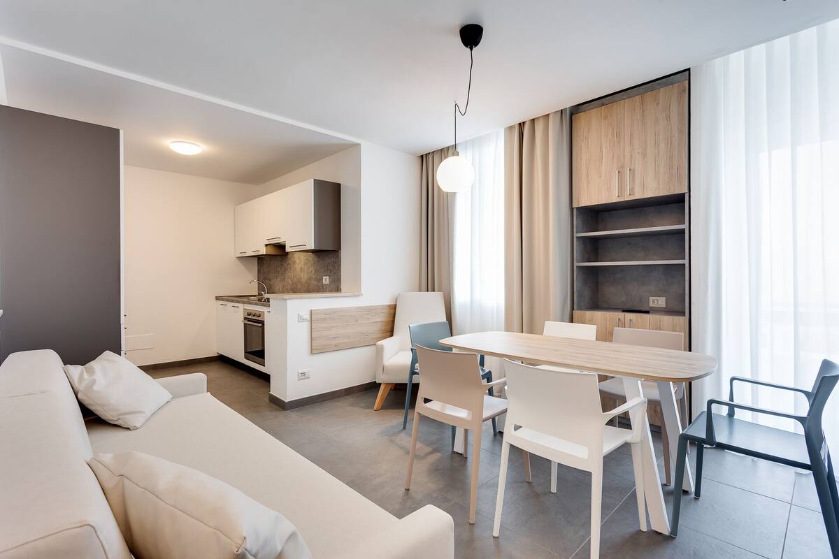 Un apartamento moderno con sala de estar, comedor, kitchenette y un gran ventanal con cortinas.