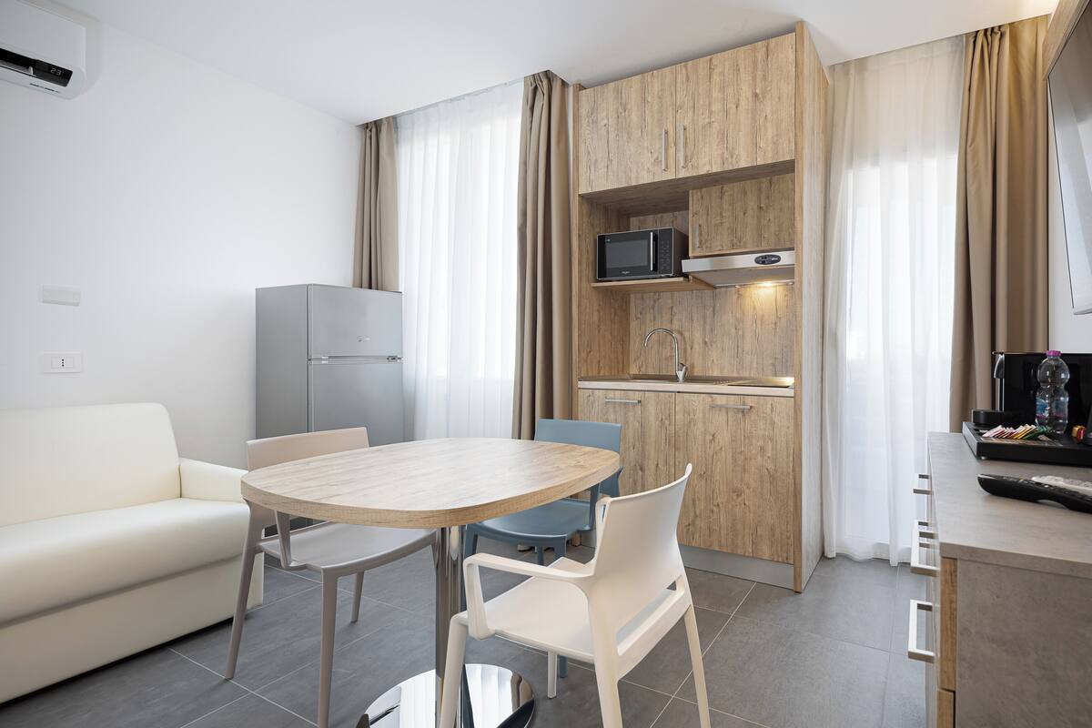 Una cocina moderna con microondas, lavamanos y armarios de madera. Hay una zona de comedor con mesa y sillas.