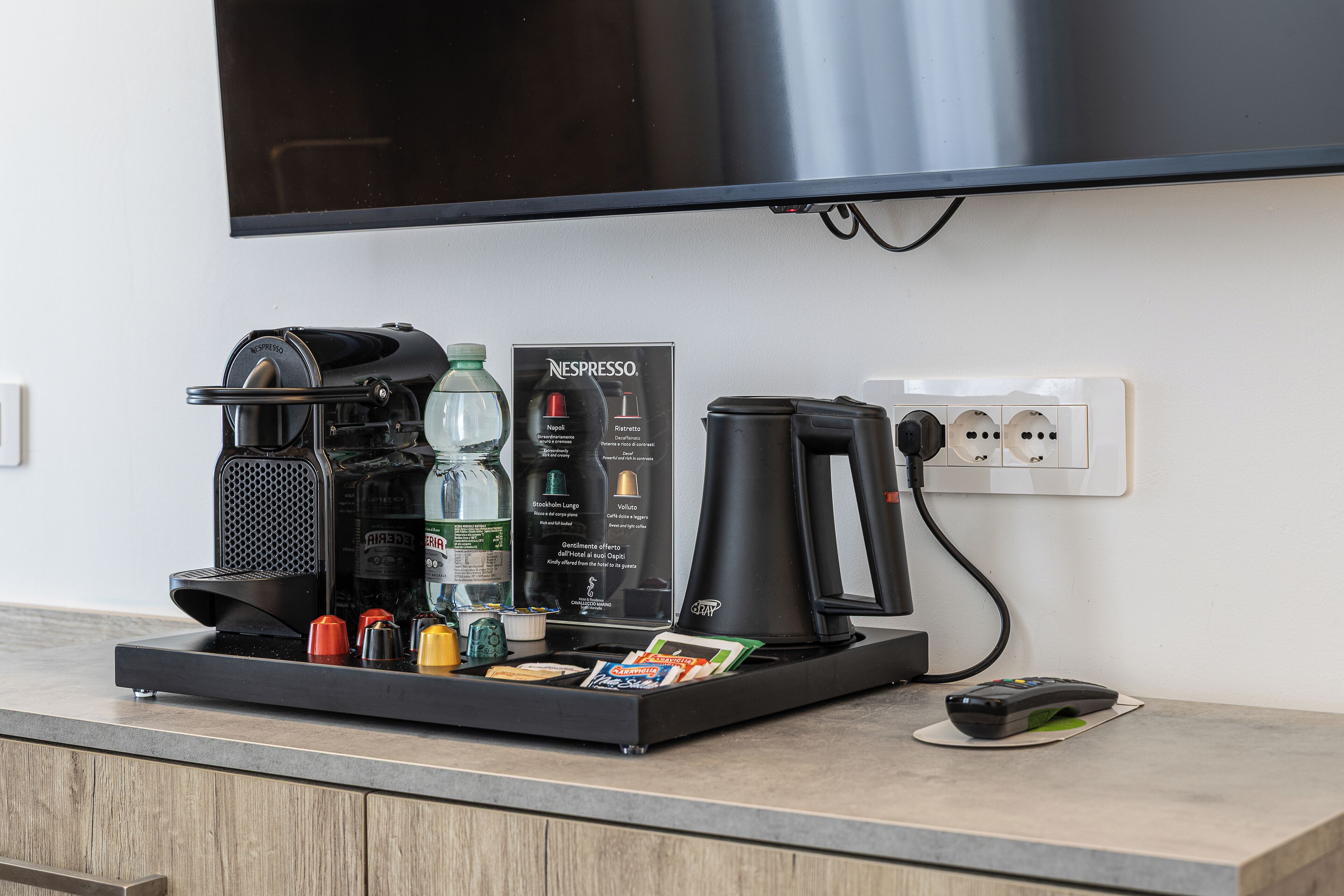 Eine Kaffeestation mit einer Nespresso-Maschine, Wasserflaschen und einer Fernbedienung auf einer Arbeitsplatte.