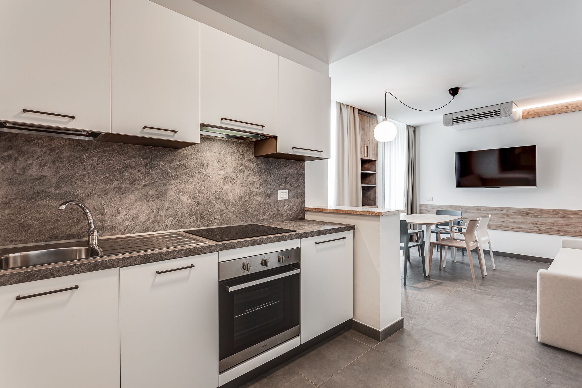 A modern kitchen with white cabinets, a granite backsplash, stainless steel appliances, and a dining area with a table and chairs.