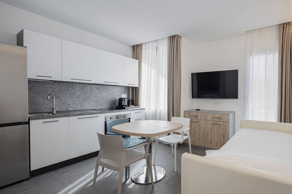 Una habitación de hotel moderna con kitchenette, una mesa de comedor redonda y un televisor de pantalla plana.