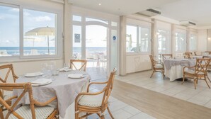 Un comedor con mesas y sillas, ventanas amplias con vistas al océano y un ventilador de techo.