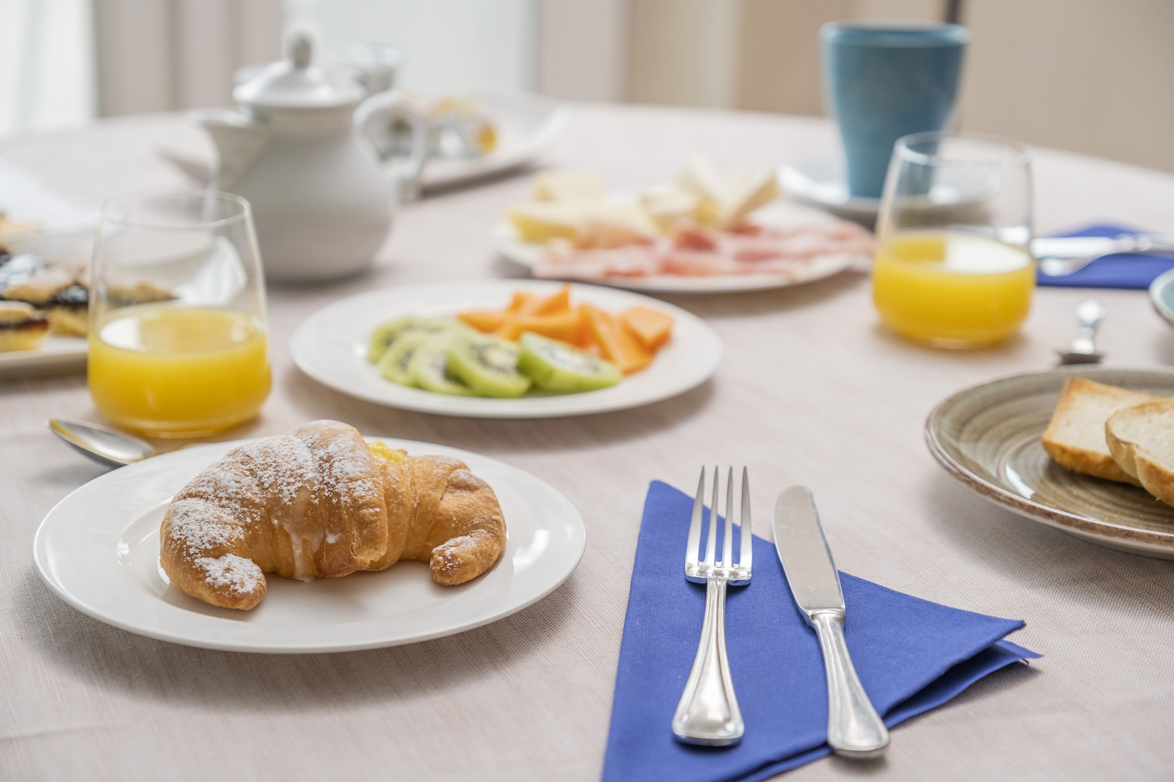 Une table dressée pour le petit-déjeuner, avec des croissants, des fruits et du jus.