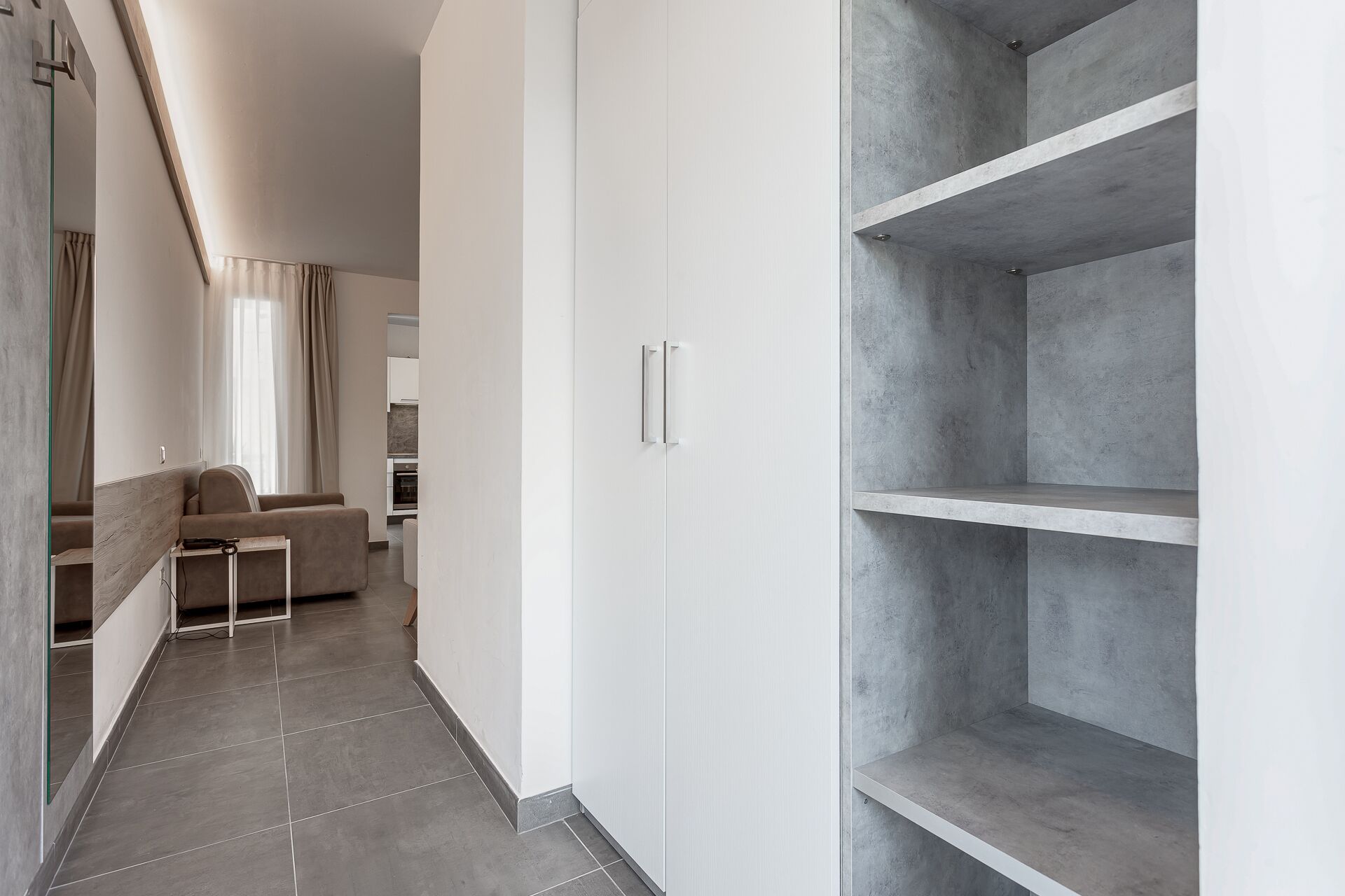 A modern interior with a minimalist design, featuring a sofa, a white wardrobe, and grey shelving units.