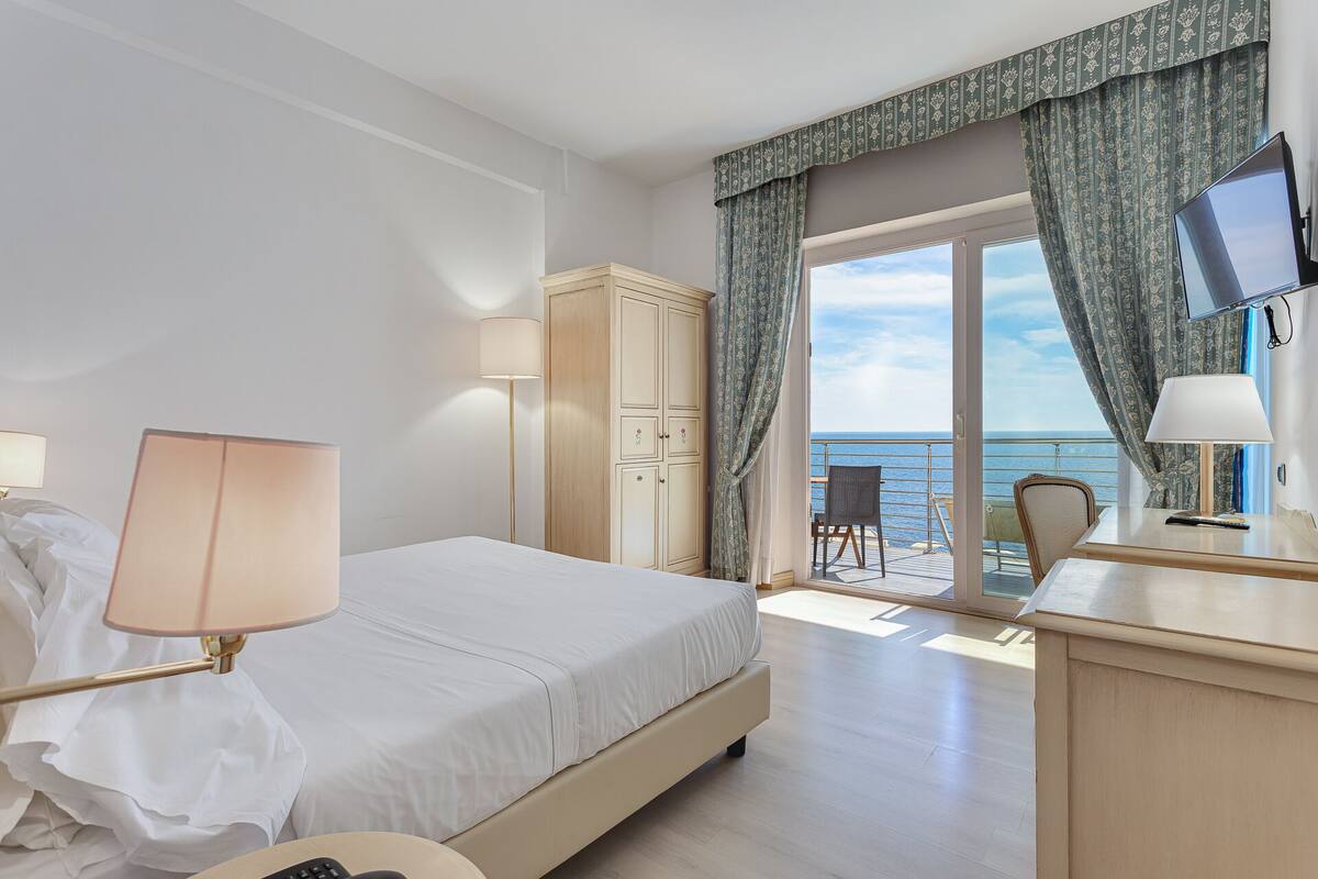Una habitación de hotel con cama, escritorio, silla, armario y vista al mar.