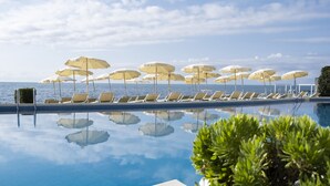 Una piscina con sillones de descanso y sombrillas, reflejando el cielo y el agua.