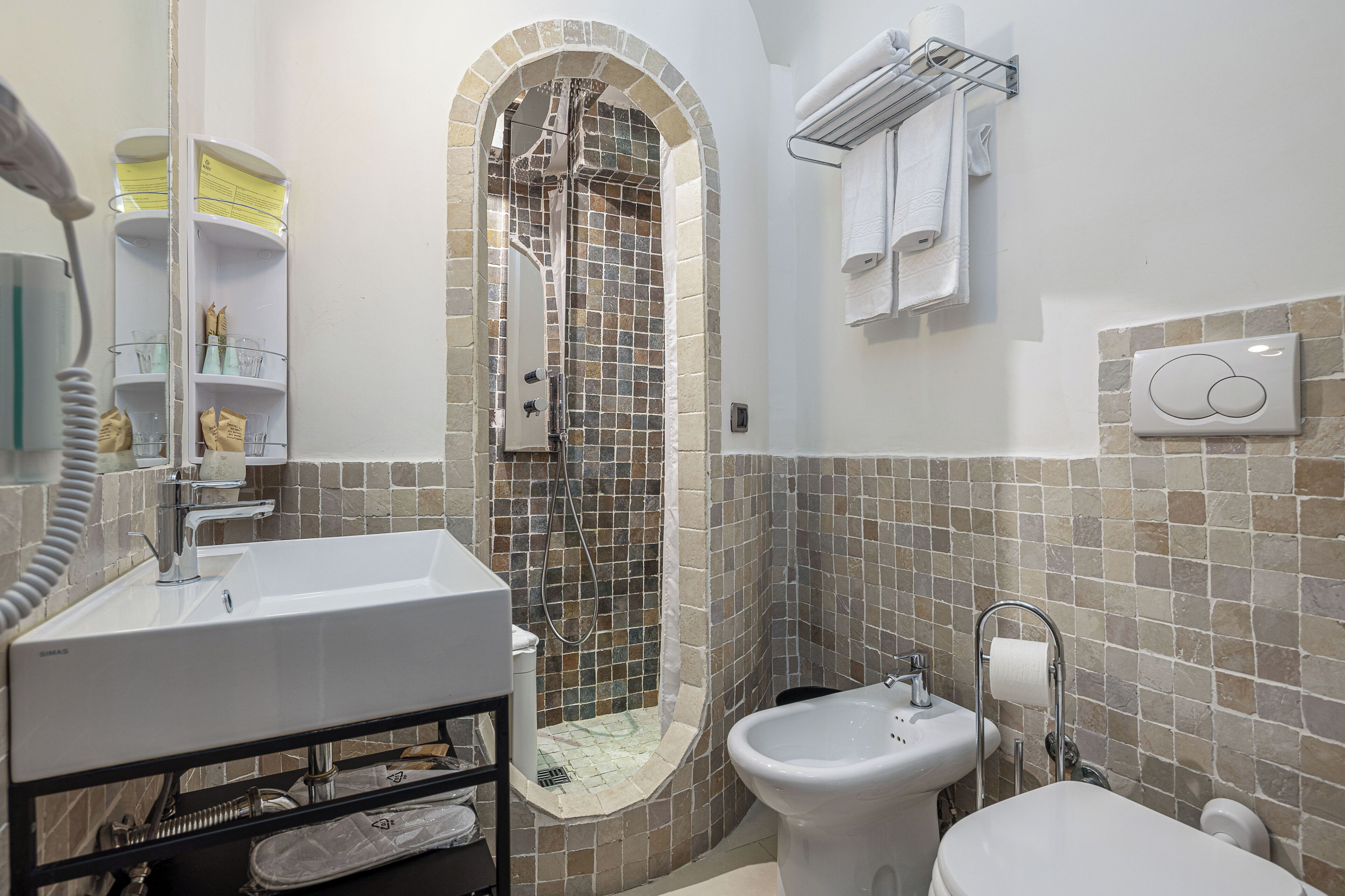 A bathroom with a shower, sink, bidet, and a tiled wall.