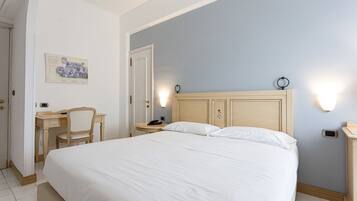 A hotel room with a large bed, a desk, a chair, and a small table.