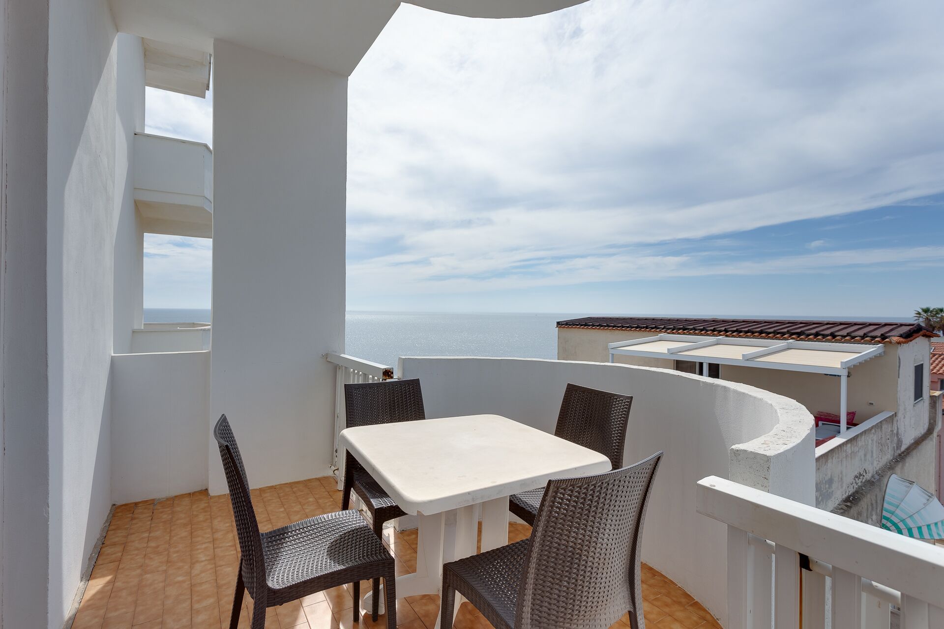 Ein Balkon mit weißem Tisch und Korbstühlen, mit Blick auf die Küste.