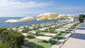 Un área de descanso en la playa con filas de tumbonas y sombrillas, vista despejada al mar y un camino empedrado.