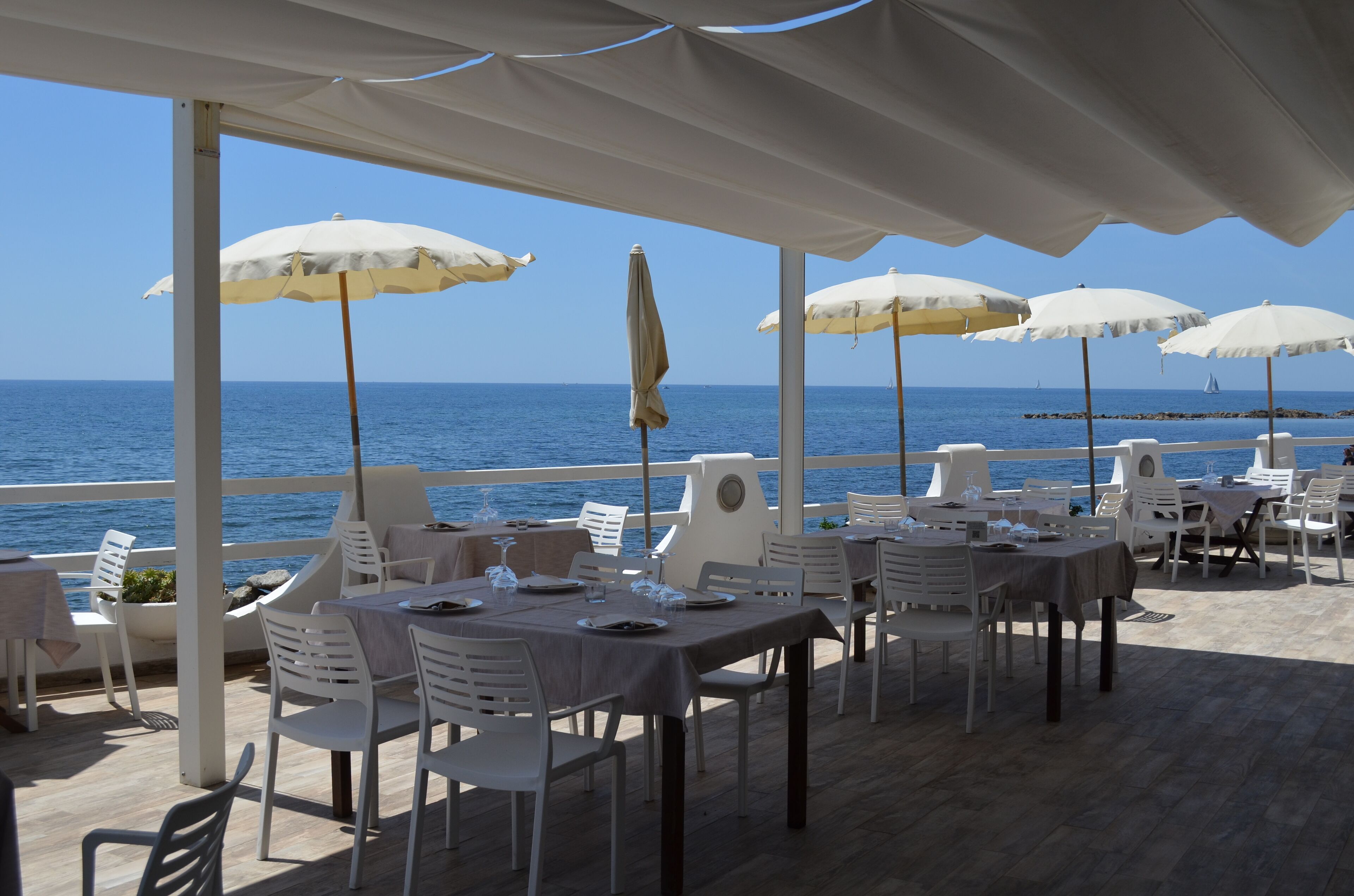 Un restaurant en bord de mer avec une terrasse, des parasols blancs et des tables dressées pour le dîner.