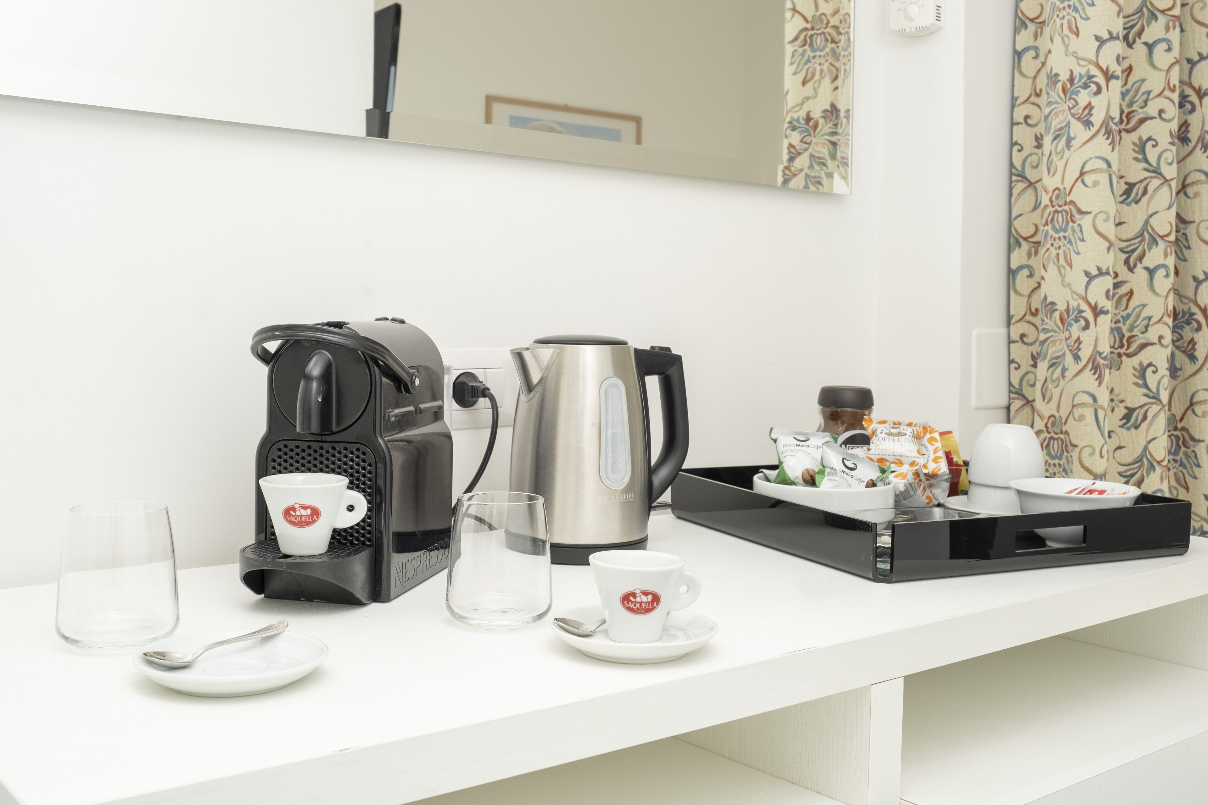 A kitchenette with a coffee maker, kettle, and a tray with a cup and saucer.