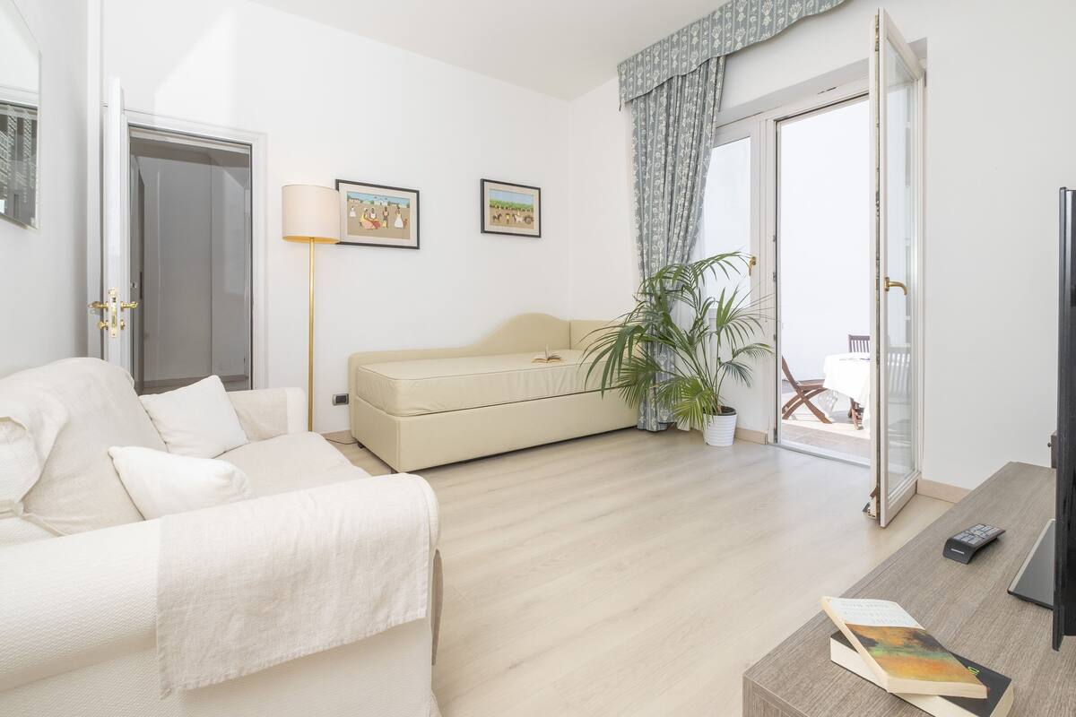 Una sala de estar moderna con un sofá color beige, una mesa de centro con un libro, una lámpara de pie y una planta en maceta.