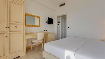 A bedroom with a bed, a desk with a chair, a wardrobe, a television, and a door leading to another room.