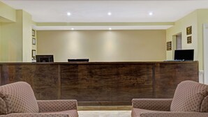 Un espace d’accueil comprenant un comptoir de réception en bois, deux fauteuils à motifs et un téléviseur à écran plat.