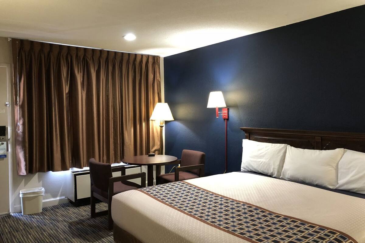 A hotel room with a bed, a desk, a chair, a lamp, and a window with curtains.