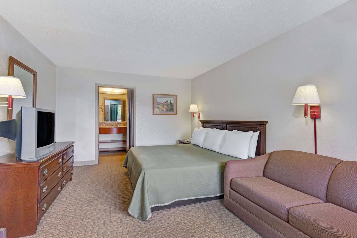 A hotel room with a bed, a sofa, a TV on a dresser, and a mirror.
