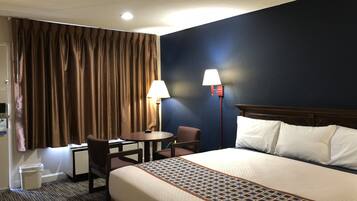 A hotel room with a bed, a desk, a chair, a lamp, and a window with curtains.