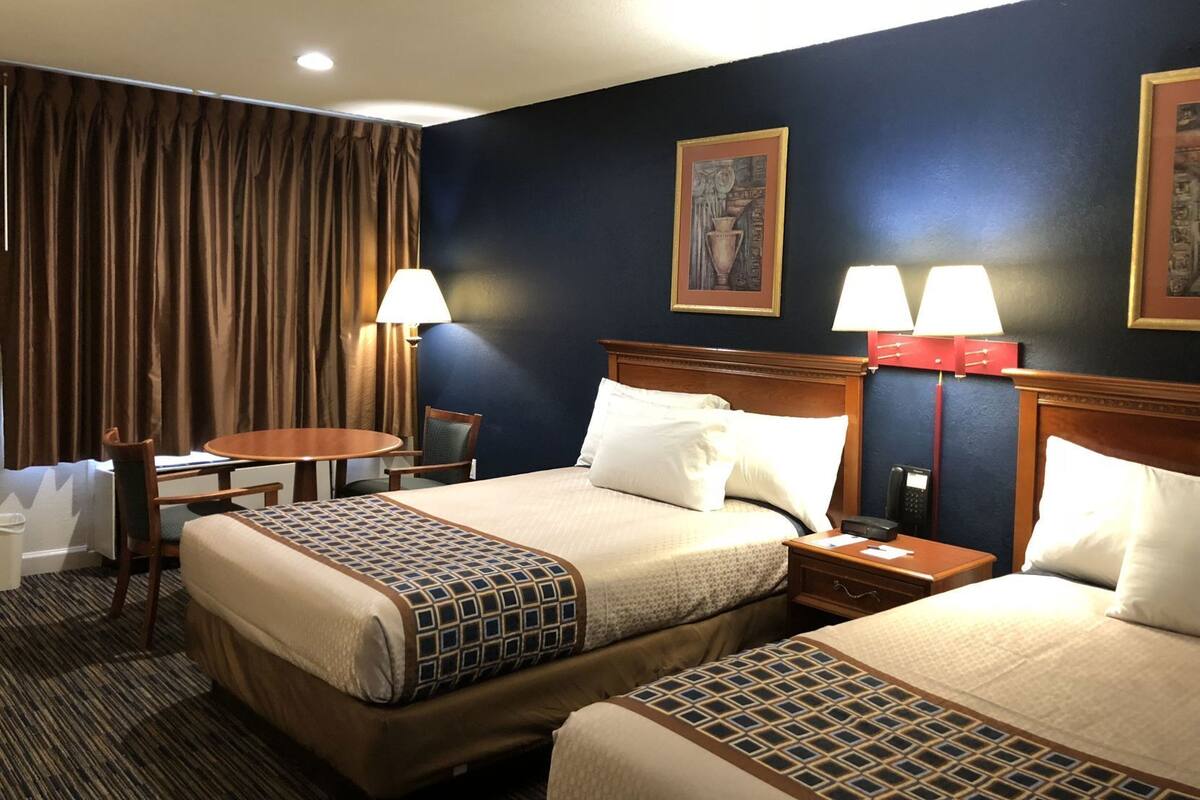 A hotel room with two beds, a desk, a chair, a lamp, and a painting on the wall.