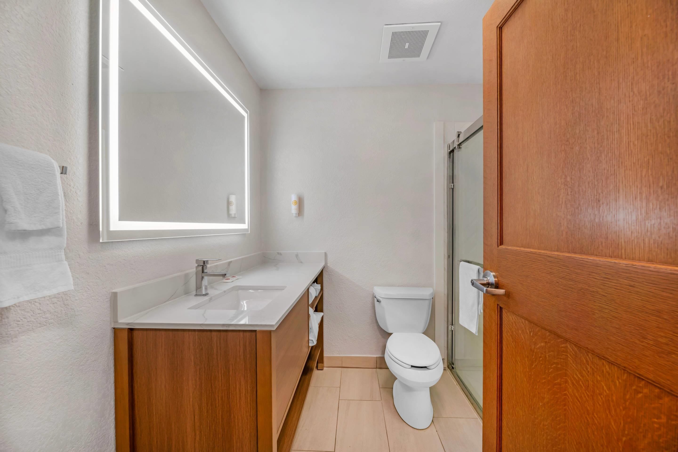 Un baño moderno con tocador de madera, lavamanos blanco e inodoro.