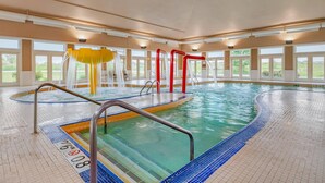 An indoor swimming pool with clear water, tiled floor, and safety railings.
