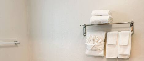 A bathroom with a toilet, grab bars, a towel rack with towels, and toilet paper.