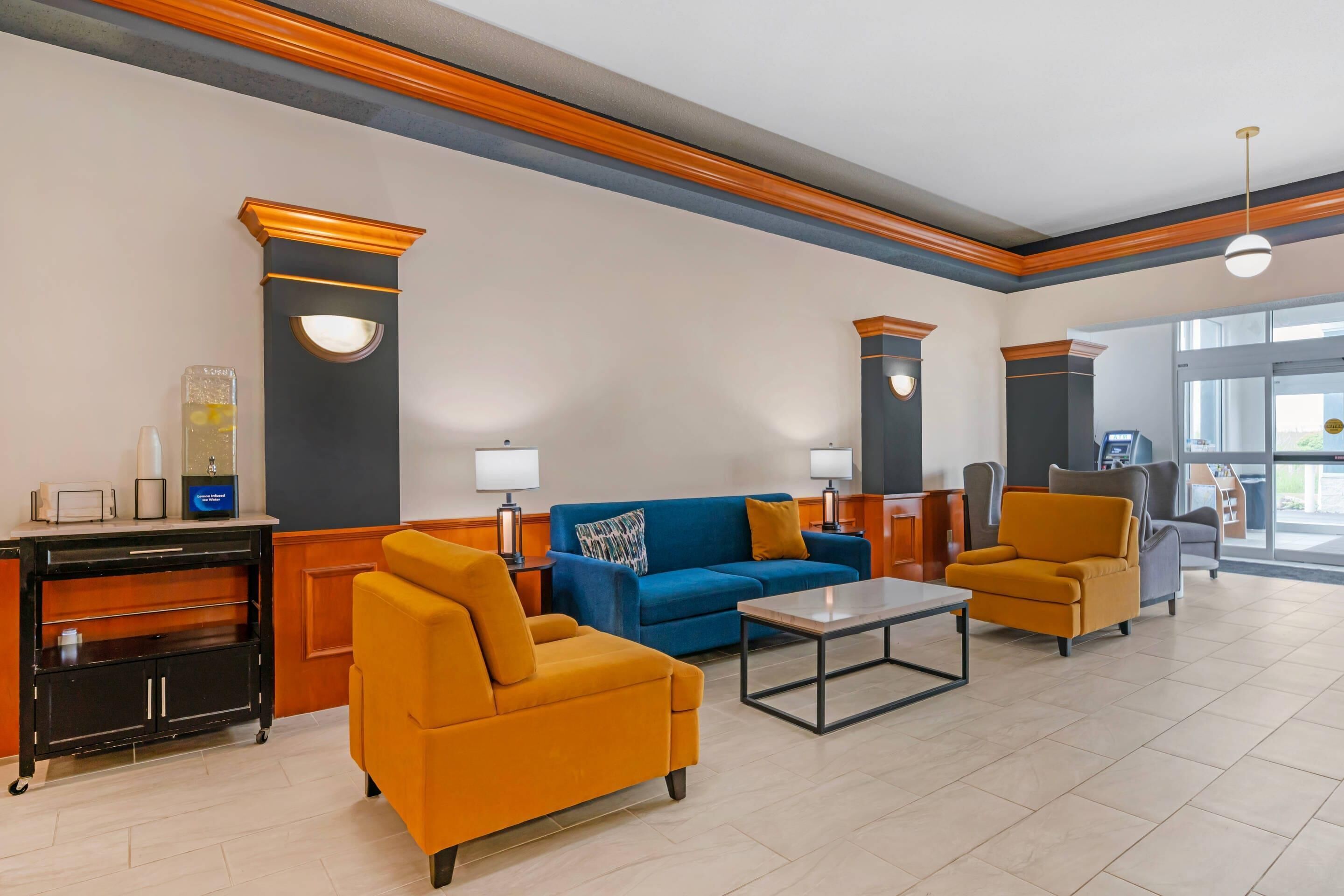 A lobby with a blue sofa, yellow armchairs, a coffee table, and a reception desk with a counter and a glass display.
