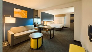 A hotel room with a sofa, a small round table, a bed, a desk, and a lamp.