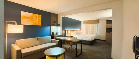 A hotel room with a sofa, a small round table, a bed, a desk, and a lamp.