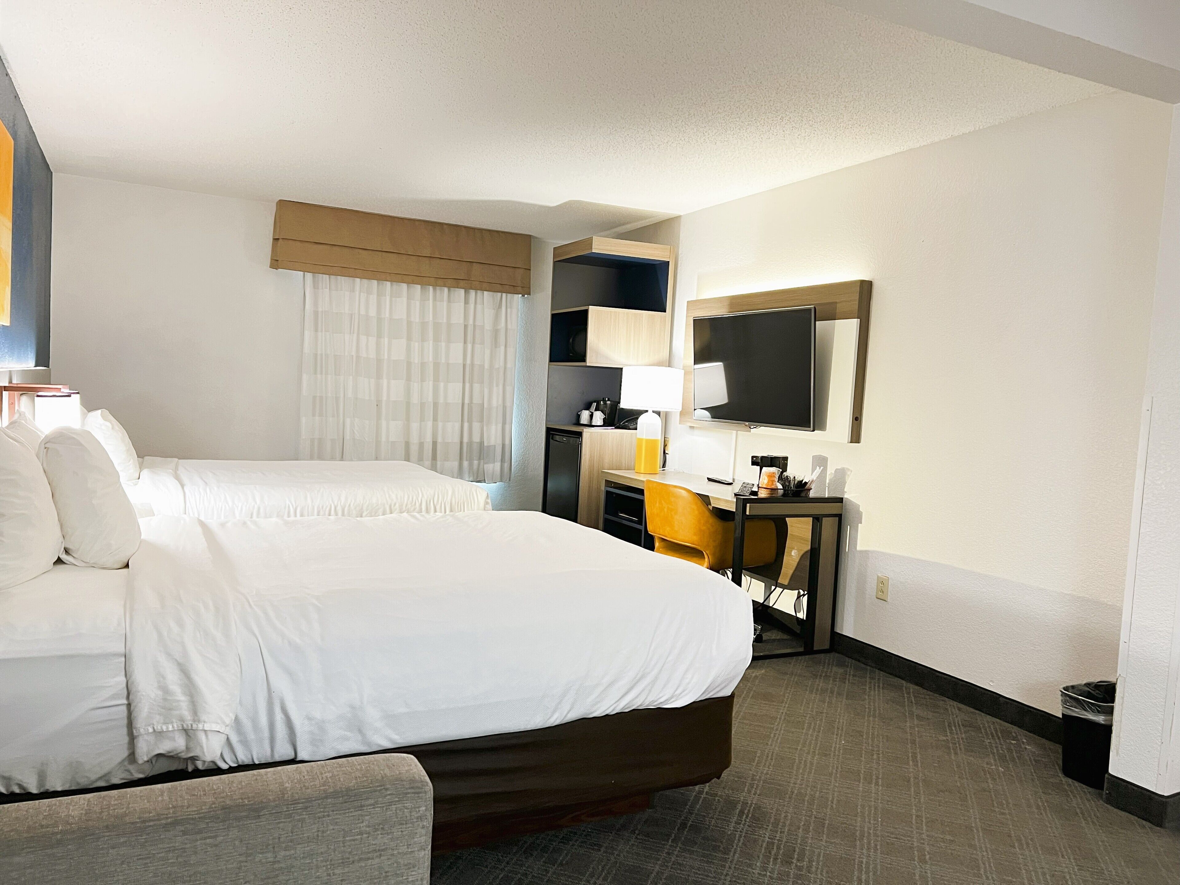 Een hotelkamer met een groot bed, een bureau met stoel, een aan de muur bevestigde televisie en een kleine prullenbak.