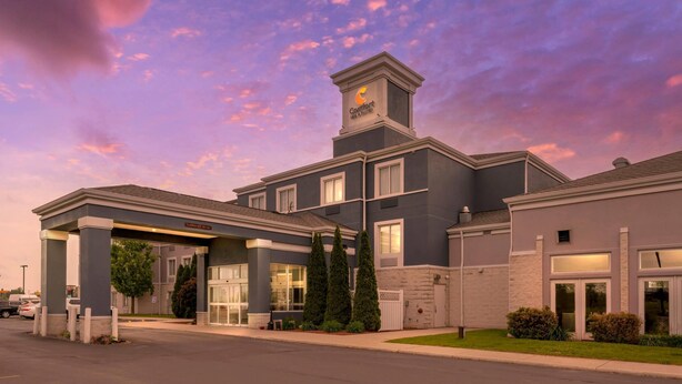A hotel with a modern design, featuring a prominent tower with the hotel name, a covered entrance, and a well-maintained lawn.