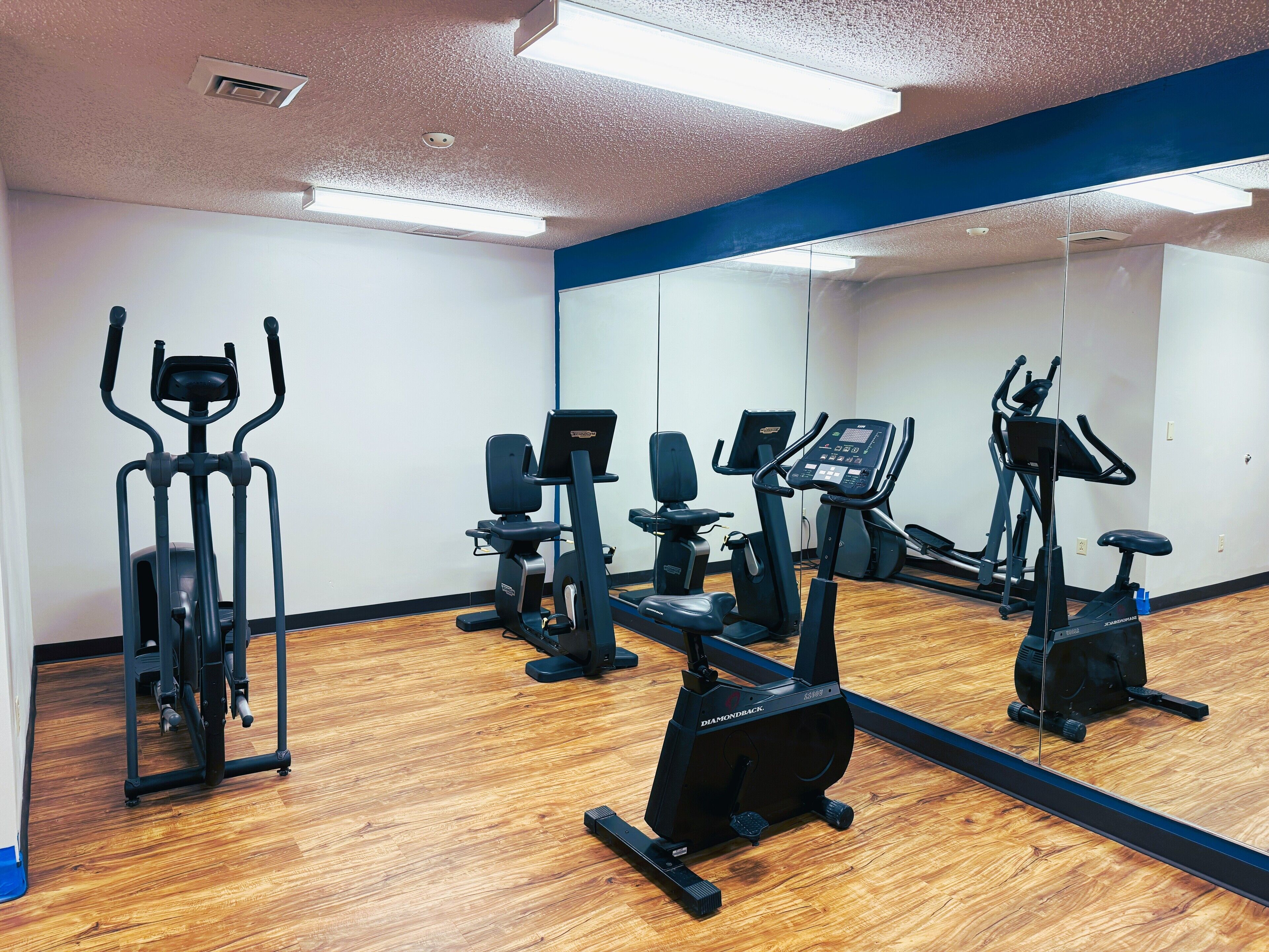 A gym with various exercise equipment, a large mirror, and wooden flooring.