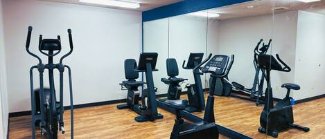 A gym with various exercise equipment, a large mirror, and wooden flooring.