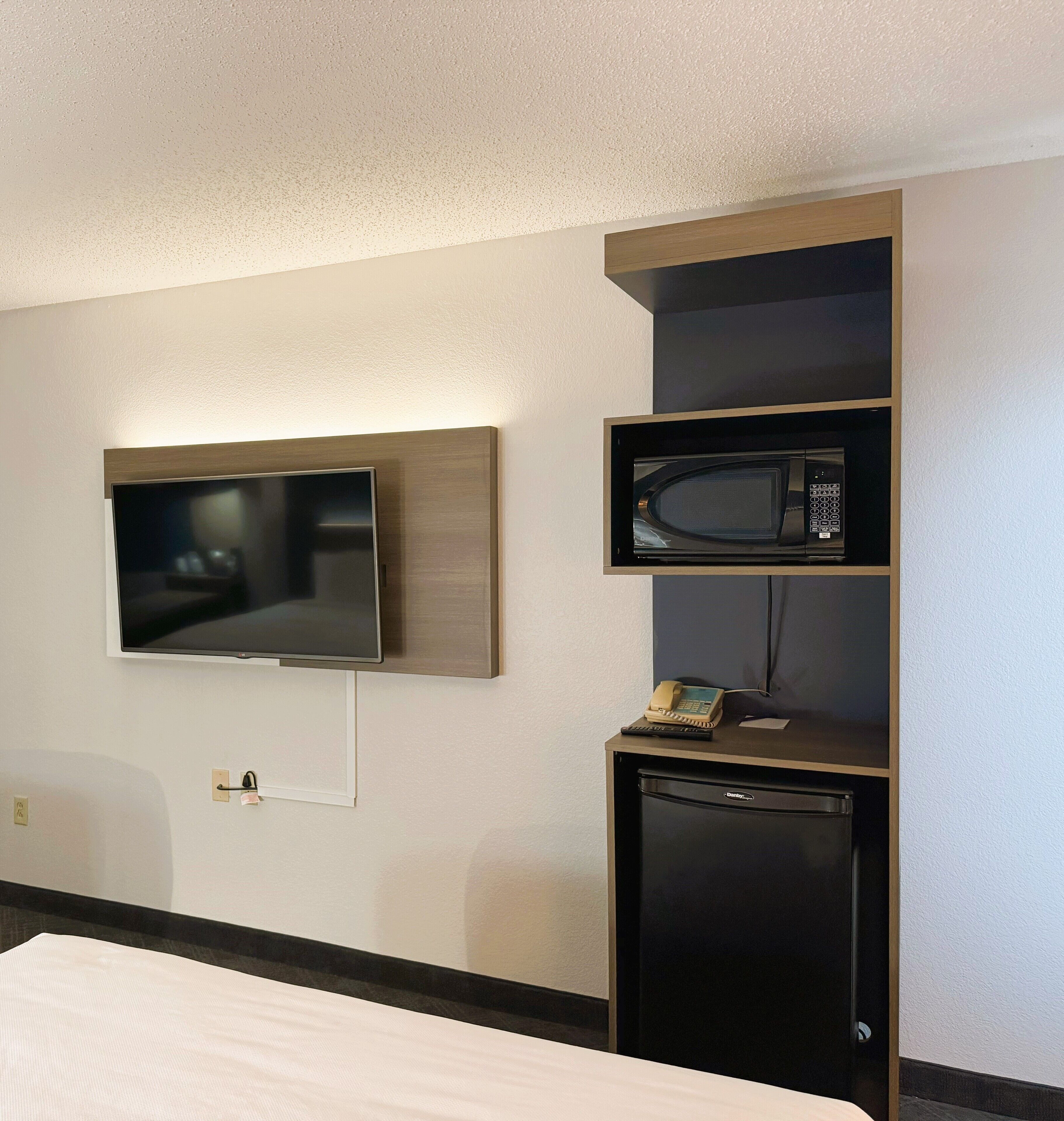 A hotel room with a flat-screen TV mounted on the wall, a microwave, and a mini fridge.