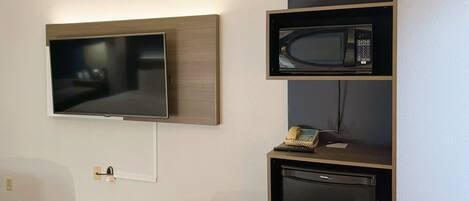 A hotel room with a flat-screen TV mounted on the wall, a microwave, and a mini fridge.