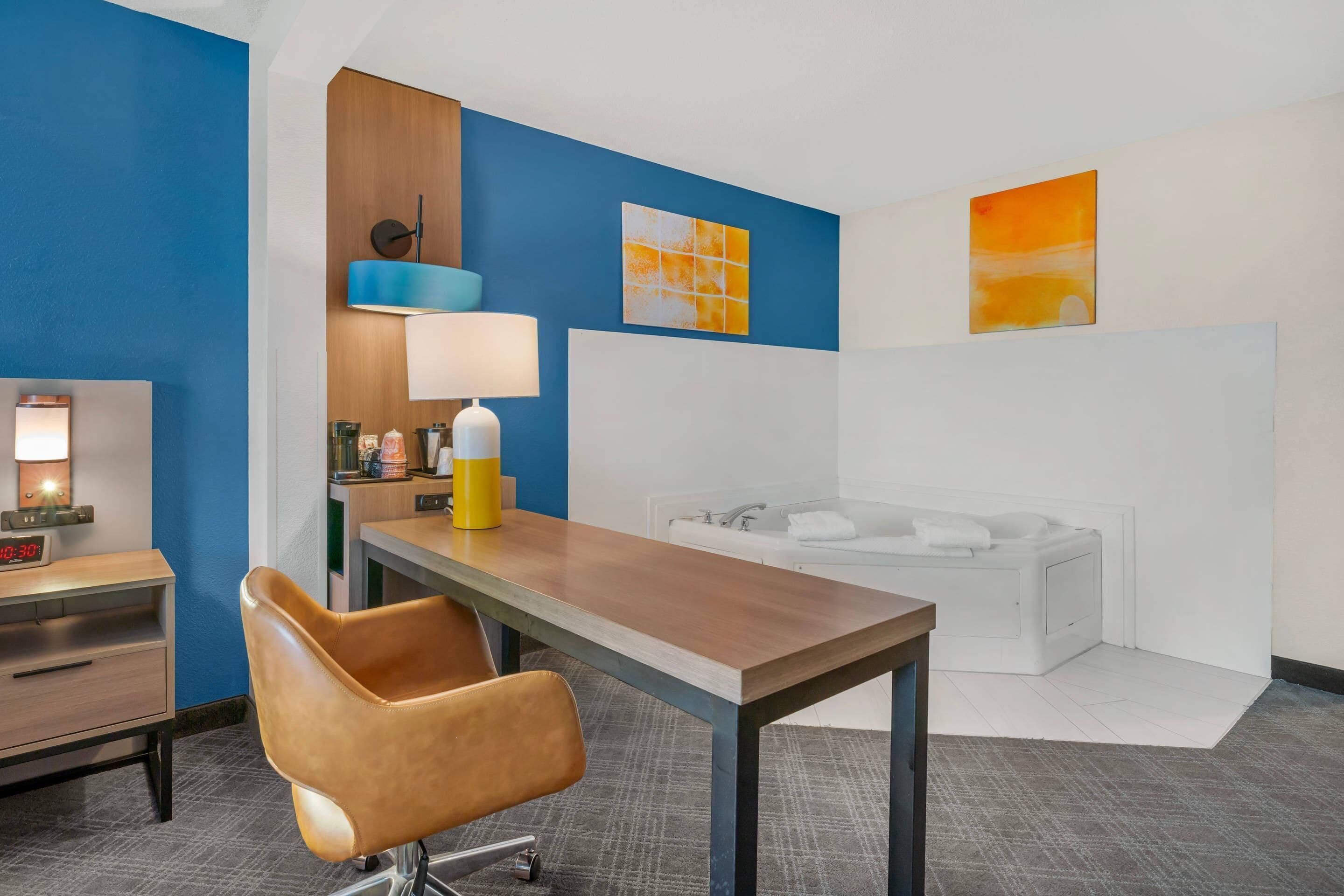 A hotel room with a wooden desk, a brown leather chair, a white bathtub, and a blue accent wall.