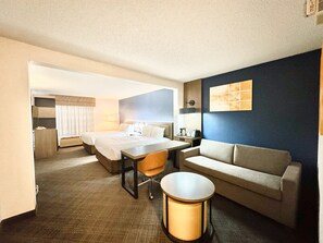 A hotel room with a bed, a desk, a chair, a sofa, and a small table.