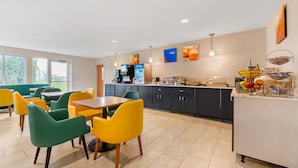 A modern dining area with a long table and colorful chairs, a kitchen with dark cabinets, and a fruit display.