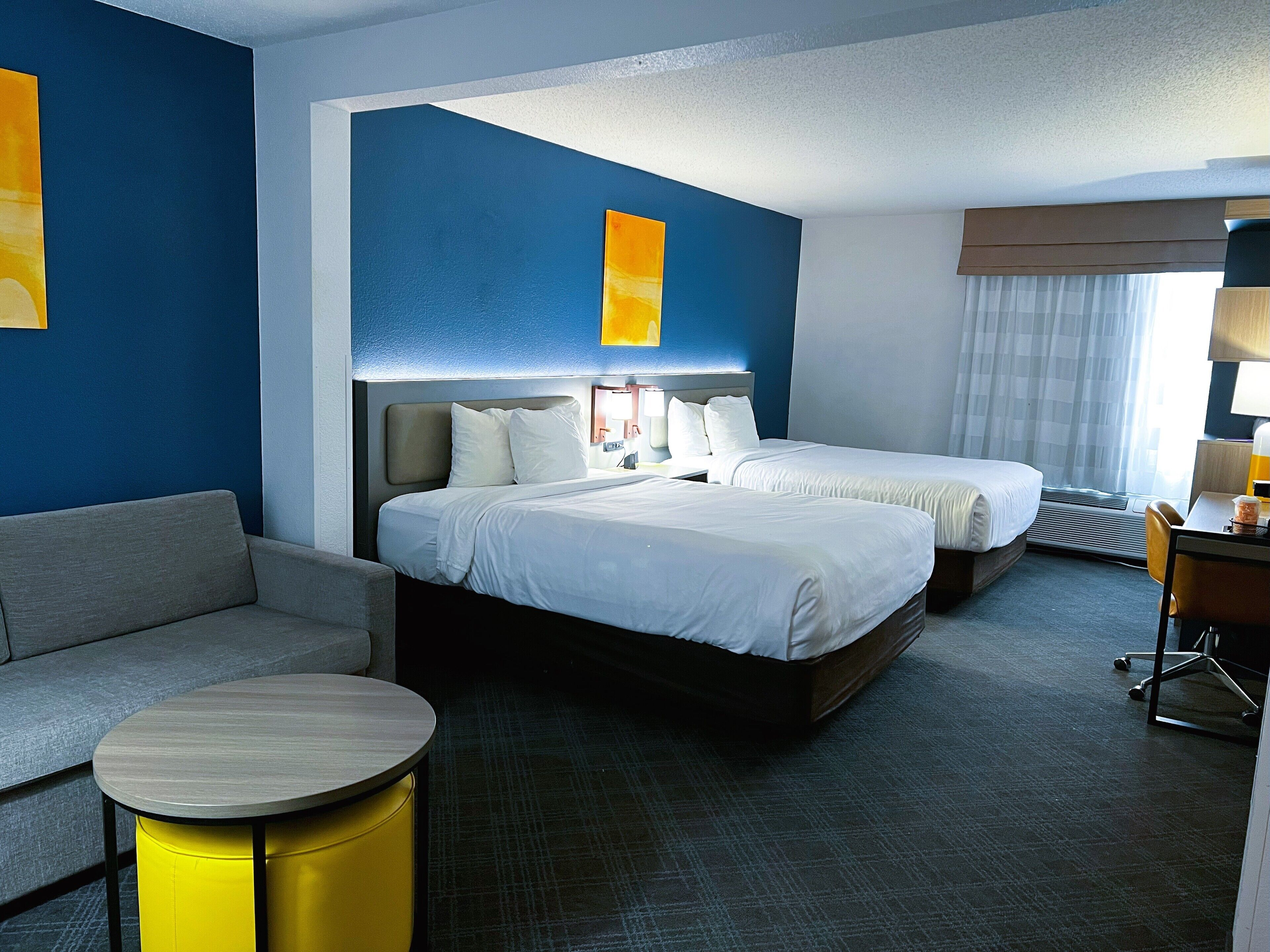 Habitación de hotel con dos camas, un sofá, una mesita redonda y un escritorio con una silla.