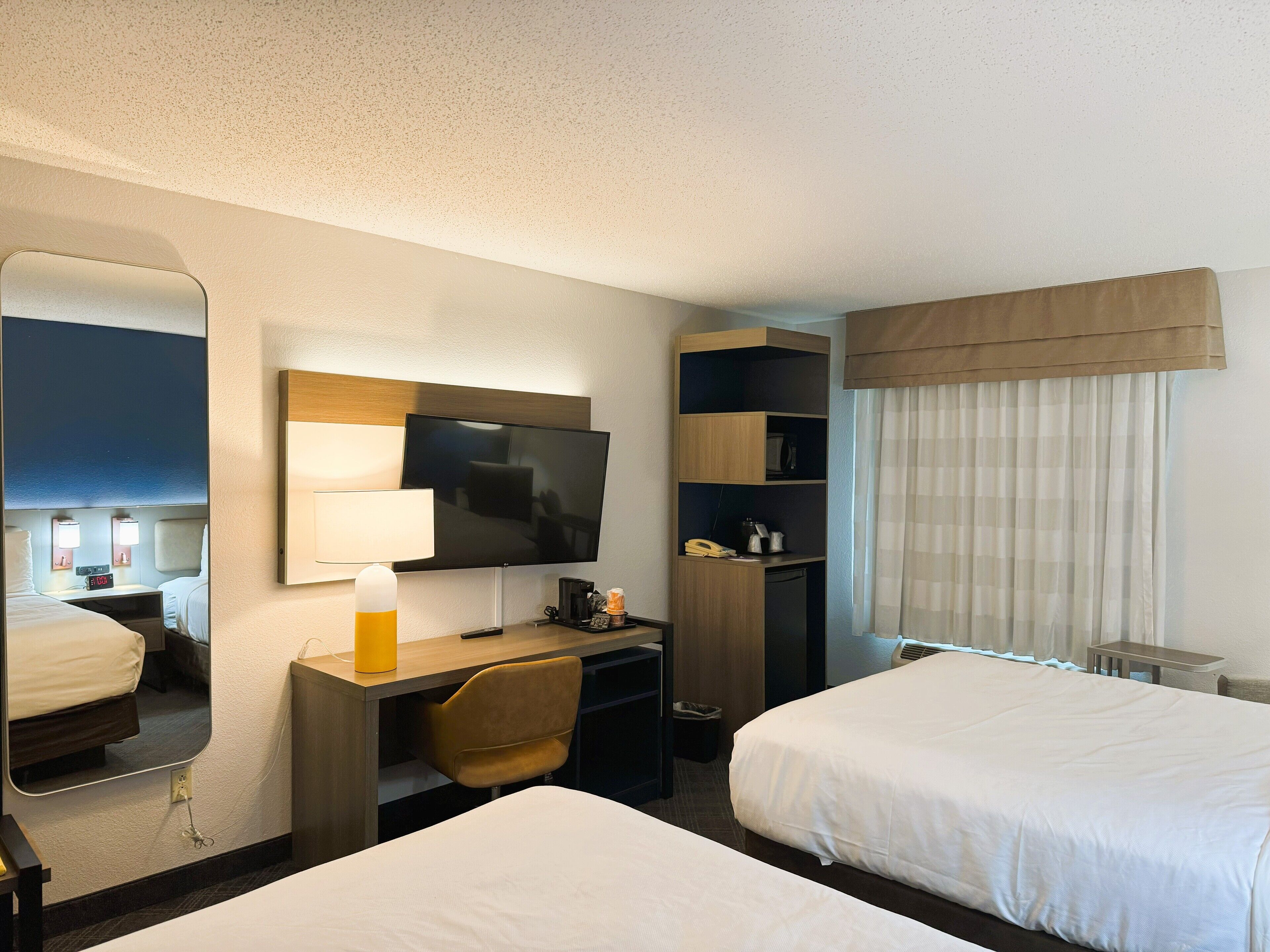 Een hotelkamer met twee bedden, een bureau met een televisie, een stoel en een kledingkast.