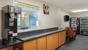 A kitchenette with a coffee machine, a refrigerator stocked with beverages, and a seating area with chairs.