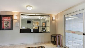 A hotel reception area with a reception desk, a large mirror, a framed picture, a small stool, and a glass door with a caution sign.