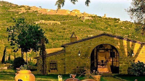 A rustic outdoor dining area with stone walls, a table, and wicker chairs. - Relais Villa Baldelli (Cortona)