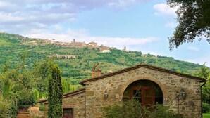 A stone building with a large arched doorway, surrounded by greenery and a hillside in the background. - Relais Villa Baldelli (Cortona)