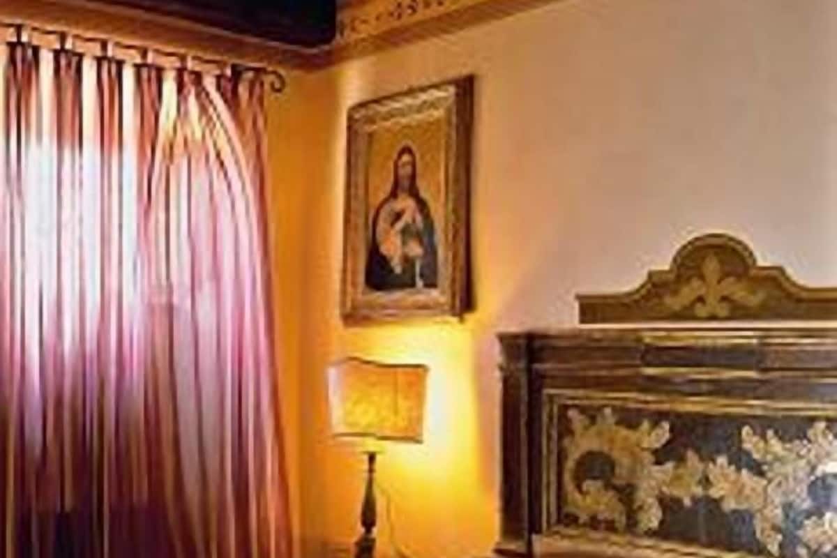 Un dormitorio con cama, mesita de noche, lámpara, un cuadro en la pared y ventana con cortinas.