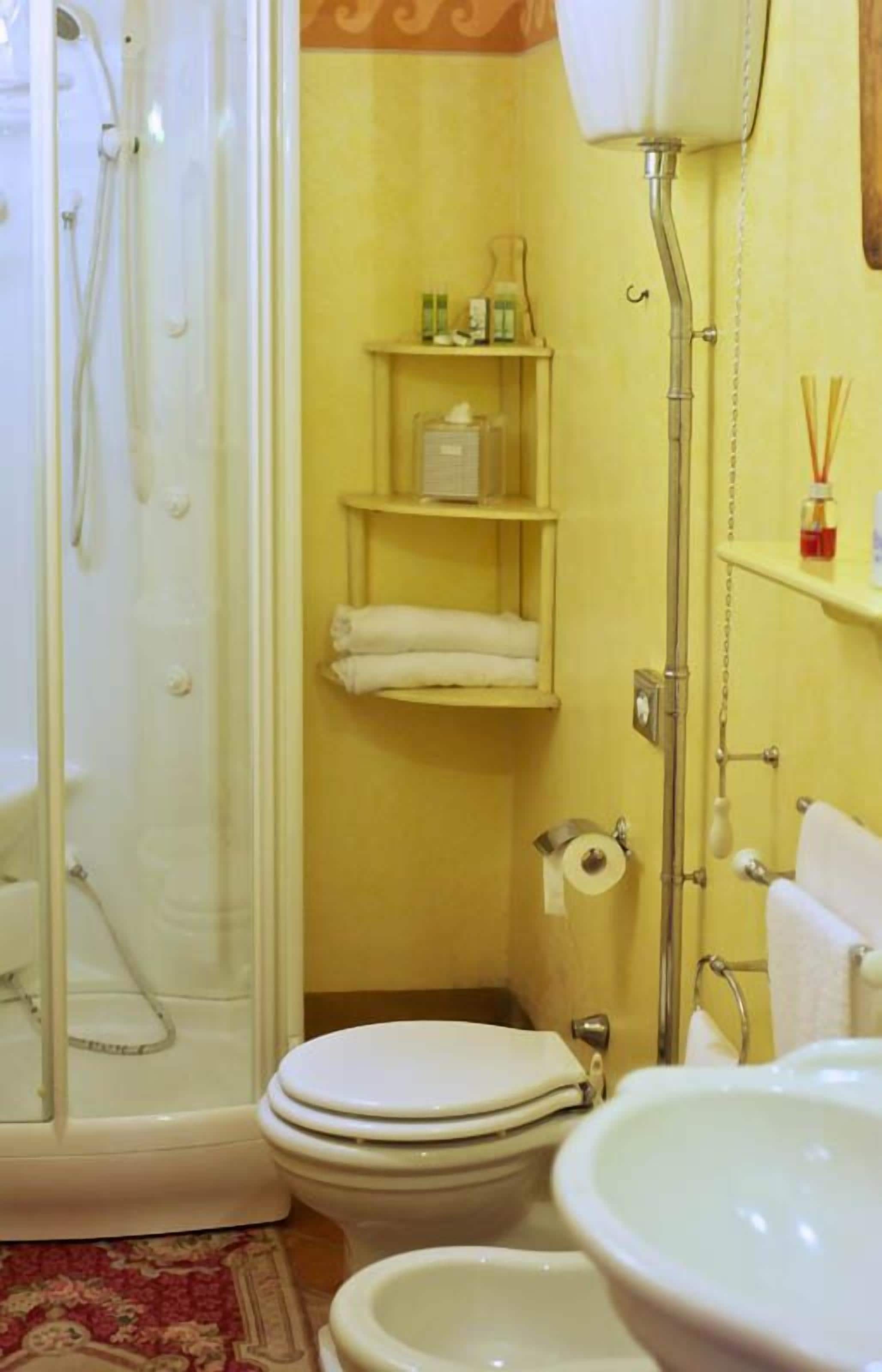 A bathroom with a glass-enclosed shower, a toilet, a sink, and shelves with toiletries.