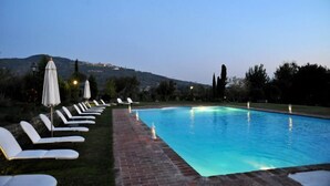 A swimming pool with lounge chairs and umbrellas, surrounded by a brick pathway and greenery. - Relais Villa Baldelli (Cortona)