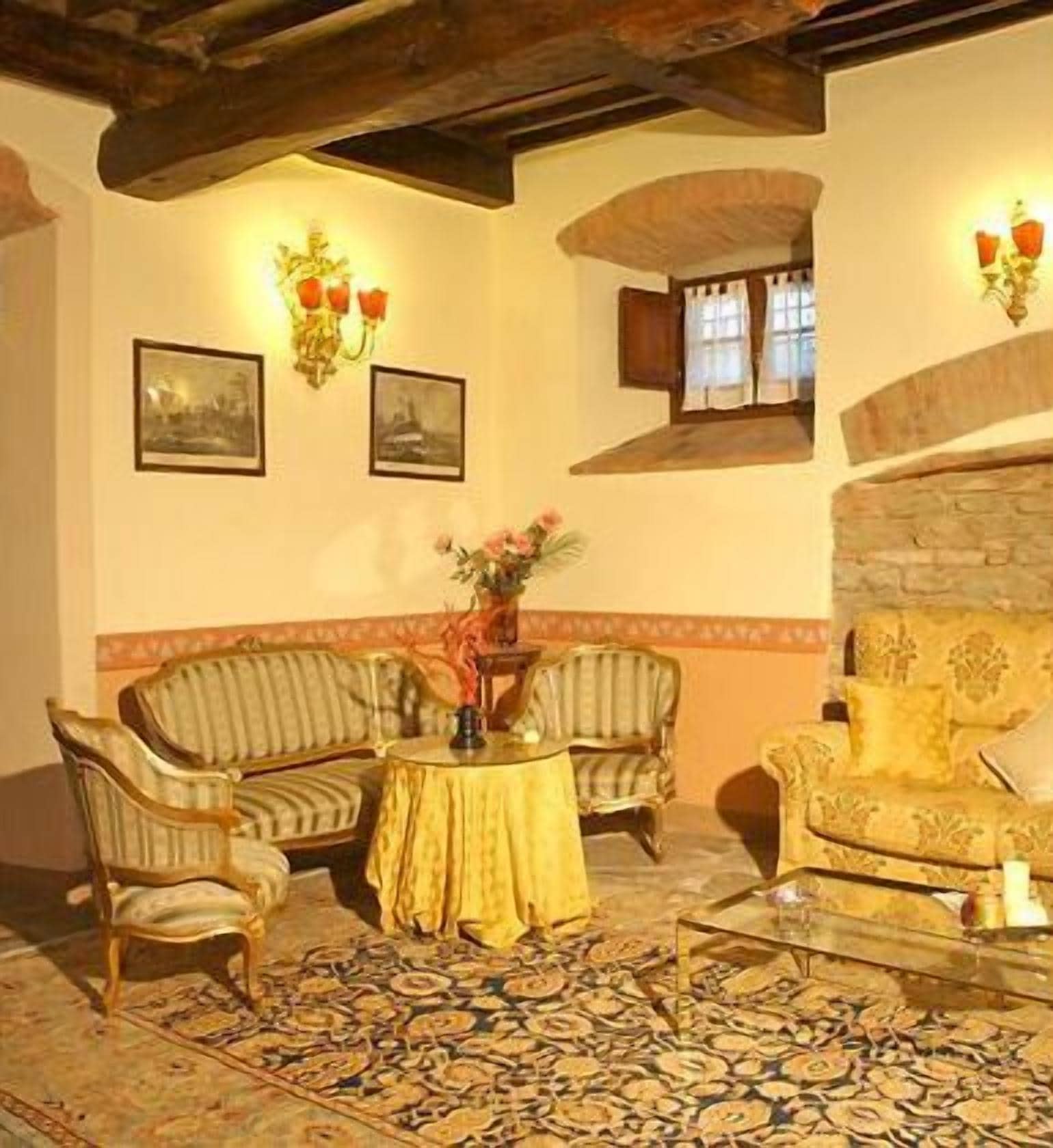 A cozy living room with a patterned rug, two armchairs, a sofa, and a small table with a vase of flowers.