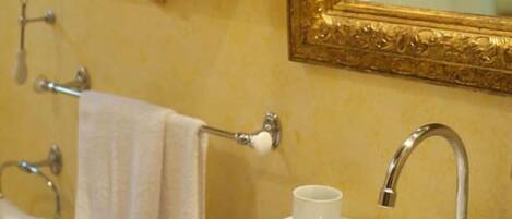 A bathroom with a sink, mirror, and towel rack. There is a shelf with toiletries and a decorative flower painting on the wall.