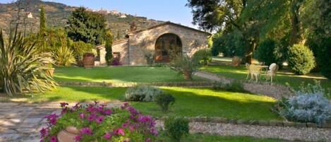 A stone building with a garden, a pathway, and a hill in the background.